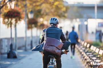 Ein Mann im Businessoutfit und mit Umhängetasche fährt auf dem Rad zur Arbeit