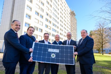 Die Projektpartner des Wist-Heims und der Linz-Energieservice GmbH stehen vor dem Wist-Heim und halten ein Solarpaneel