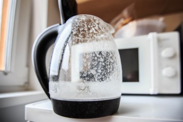 Verkalkter Wasserkocher aus Glas steht auf einer Küchenzeile vor einer Mikrowelle