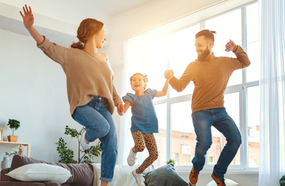 Mutter, Vater und Kind in Wohnung hüpfen auf der Couch und lachen.