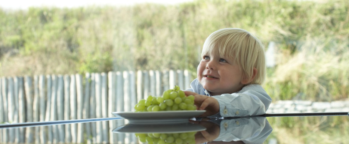 Ein Junge nimmt sich Weintrauben aus einer Schüssel vom Tisch