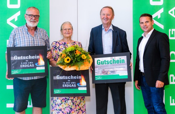 3 Männer und 1 Frau stehen nebeneinander mit Gutscheinen in der Hand und grünen Bannern dahinter.