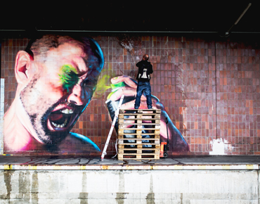 Graffitikünstler besprüht Wand im Linzer Hafen mit einem riesigen Graffiti, das einen Mann zeigt, der sich selber in die Augen sprayt. Das Werk heißt "Paint It Black 2015" und stammt vom Künstler SHED.