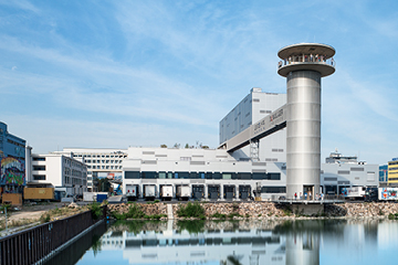 Ansicht auf den Turm neben dem Hafenbecken mit dem Hafenpark im Hintergrund.