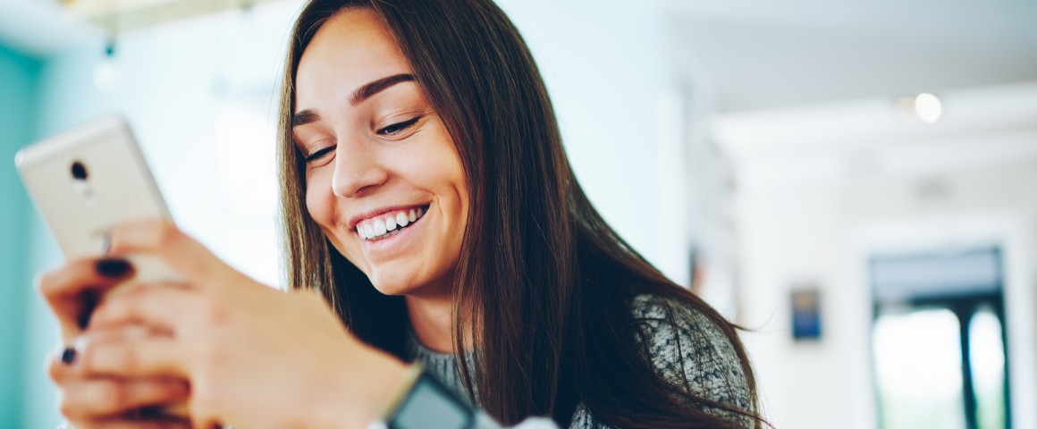 Ein Mädchen sieht lächelnd auf ihr Smartphone.