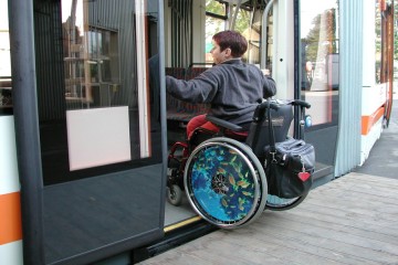 Eine junge Frau fährt mit dem Rollstuhl in eine Straßenbahn.