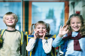 Drei Kinder (ein Junge und zwei Mädchen) winken fröhlich in die Kamera.