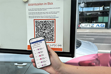 Hand mit einem Smartphone  vor einem Plakat mit einem QR-Code