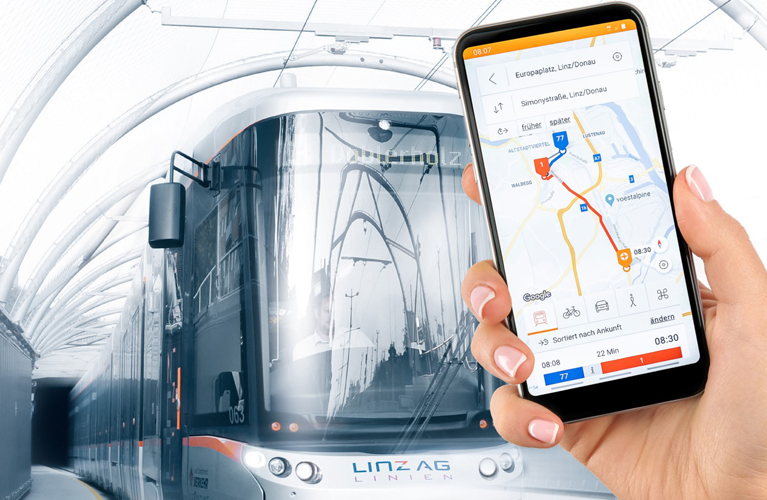 Ein Smartphone mit der Linzmobil App wird in die Kamera gehalten. Im Hintergrund ist eine Straßenbahn zu sehen.