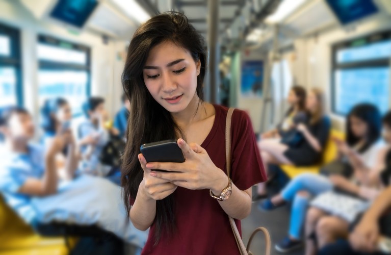 Eine Frau sieht auf ihr Smartphone in der Straßenbahn.