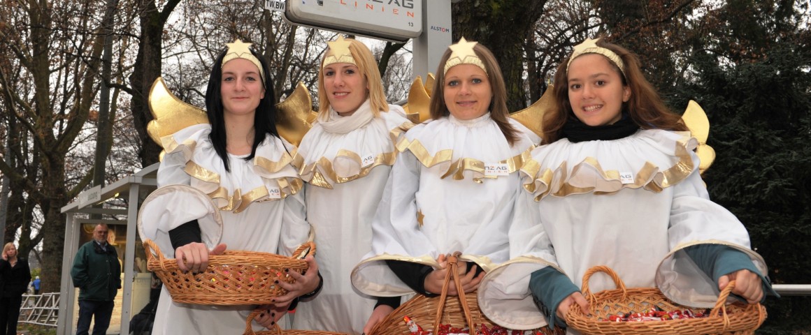 Vier Mädchen in Engelkostümierungen stehen vor einer Straßenbahnhaltestelle der LINZ AG.