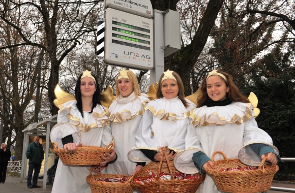 Vier Mädchen in Engelkostümierungen stehen vor einer Straßenbahnhaltestelle der LINZ AG.