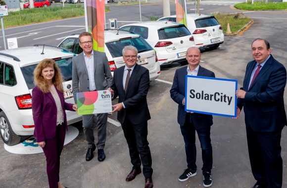 Herr Haider, Waldhör, Lugner, Hein und Frau Rinner stehen mit einem Ortschild der SolarCity vor den Tim Autos.