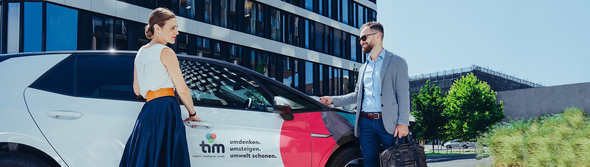 Eine Frau und ein Mann stehen vor dem tim-Auto und sind gerade dabei einzusteigen.