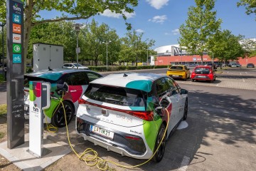 Zwei Fahrzeuge der tim-Flotte stehen am Mobilitätsknoten am Froschberg und werden geladen. Im Hintergrund ist die Tips Arena zu sehen.