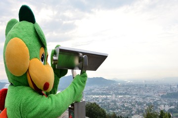 Ein kostümierter Drache blickt durch ein Fernrohr über die Stadt Linz in Oberösterreich.