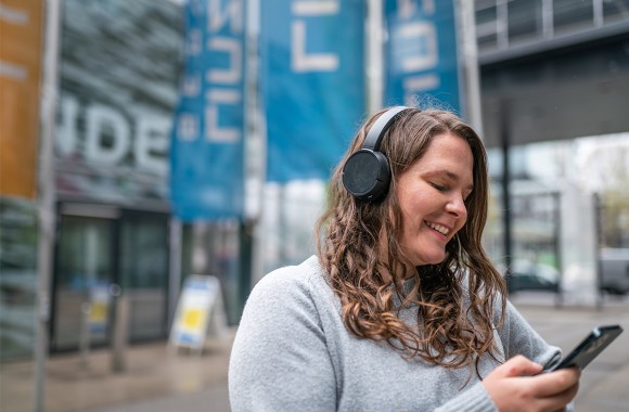 Foto einer Kundin vor dem LINZ AG Kundenzentrum, die mit Kopfhörern auf dem Smartphone Musik hört