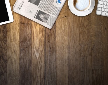 Ein Fotoausschnitt mit einem Tablet, einer Zeitung, einer Tasse Kaffee und einer Tastatur