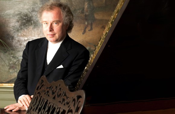 Sir Andras Schiff posiert an einem Flügel vor einem Olgemälde