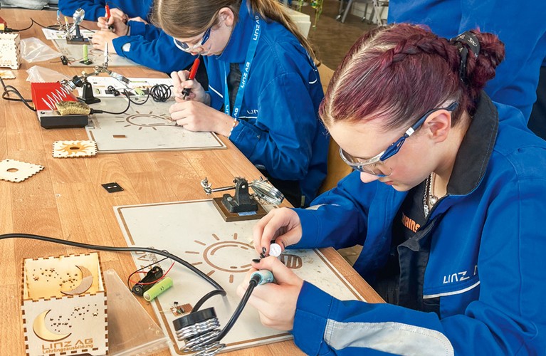 Junge Mädchen sitzen mit einer Schutzbrille an einem Tisch und löten