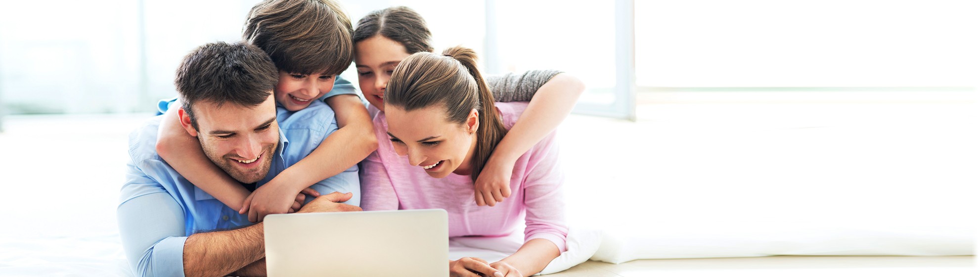 Photo einer Familien mit Vater, Mutter und 2 Kindern am Boden vor einem Laptop liegend