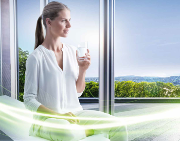 Frau sitzt mit einem Glas Wasser am Fenster und schaut auf Linz hinab
