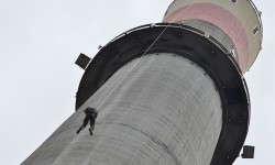 Ein Mitarbeiter der Cobra hängend an einem Seil am Kraftwerkskamin.