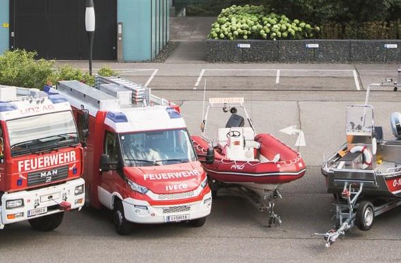 Abbildung des Fuhrparks der Betriebsfeuerwehr der LINZ AG (links großes Feuerwehrauto, daneben ein etwas kleineres, zwei Boote und rechts davon noch zwei ältere Feuerwehrautos)