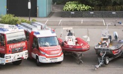 Abbildung des Fuhrparks der Betriebsfeuerwehr der LINZ AG (links großes Feuerwehrauto, daneben ein etwas kleineres, zwei Boote und rechts davon noch zwei ältere Feuerwehrautos)
