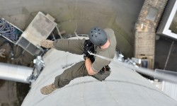 Seiltechnikübungen der Cobra am Kraftwerkskamin. Mann hängt an Seil. Aufnahme aus Vogelperspektive