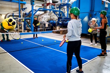 Wättchen spielt Tennis mit zwei Frauen und einem Mann in der Turbinenhalle des Fernheizkraftwerkes.
