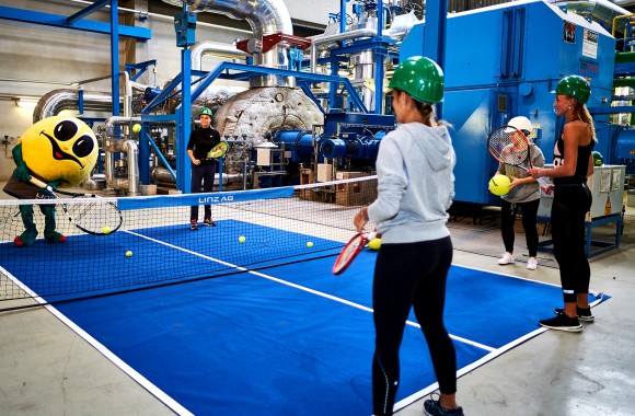 Wättchen spielt Tennis mit zwei Frauen und einem Mann in der Turbinenhalle des Fernheizkraftwerkes.