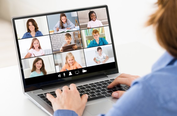 Frau sitzend vor Laptop. Auf Laptop Bildschirm sind mehrere Kinder zu sehen.