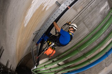 Schacht, Donaudüker, Kletterer hängt im Seil und montiert Kabelkanal.