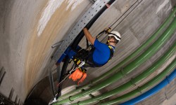 Schacht, Donaudüker, Kletterer hängt im Seil und montiert Kabelkanal.