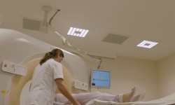 Eine Frau schiebt eine andere Person in das MR Gerät in einer Arztpraxis. Der Raum ist hell mit LED Beleuchtung ausgeleuchtet