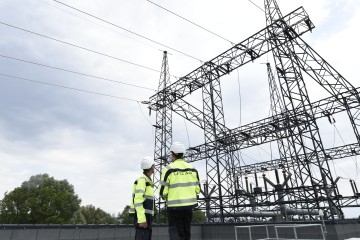 Abbildung zweier Mitarbeiter der LINZ AG in Arbeitsgewand vor einem Strommasten
