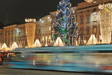 Straßenbahn fährt durch die Linzer Innenstadt, die Weihnachtsbeleuchtung ist eingeschaltet.
