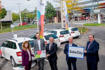 Generaldirektor Erich Haider, Vorstandsdirektorin Dr. Jutta Rinner, Herr Waldhör, Luger und Herr Hein mit der Ortstafel der SolarCity und einer Tim Mobilitätskarte vor den Tim Autos