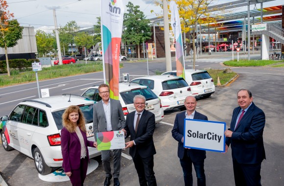 Generaldirektor Erich Haider, Vorstandsdirektorin Dr. Jutta Rinner, Herr Waldhör, Luger und Herr Hein mit der Ortstafel der SolarCity und einer Tim Mobilitätskarte vor den Tim Autos