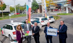 Generaldirektor Erich Haider, Vorstandsdirektorin Dr. Jutta Rinner, Herr Waldhör, Luger und Herr Hein mit der Ortstafel der SolarCity und einer Tim Mobilitätskarte vor den Tim Autos