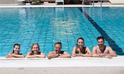 junge Erwachsene lächeln fröhlich in Kamera und lehnen am Beckenrand des Sportbeckens im Parkbad