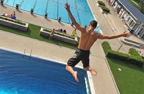 Mann springt mit ausgestreckten Armen vom Sprungturm im Parkbad