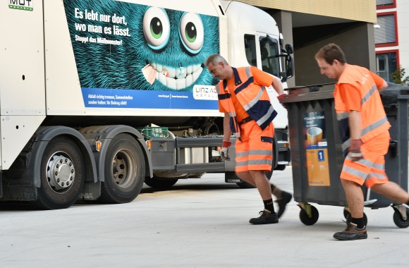 zwei Mitarbeiter der LINZ AG ABFALL bringen Mülltonne zum Lastkraftwagen