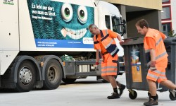 zwei Mitarbeiter der LINZ AG ABFALL bringen Mülltonne zum Lastkraftwagen