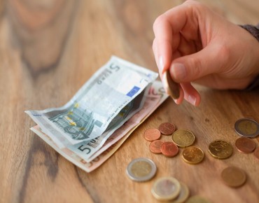 Eine Hand zählt Euromünzen und Euroscheinen auf einem Tisch.