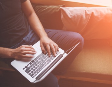 Ein Mann sitzt auf einer Couch und hält ein Notebook in den Händen.