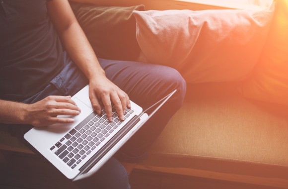 Ein Mann sitzt auf einer Couch und hält ein Notebook in den Händen.