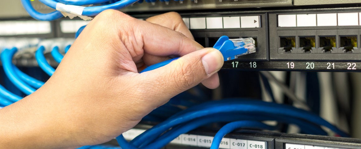 Eine Hand steckt in einem Serverschrank eine Kabel aus einem Server Rack