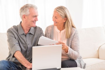 Älteres Paar sitzt mit Dokumenten vor dem Computer